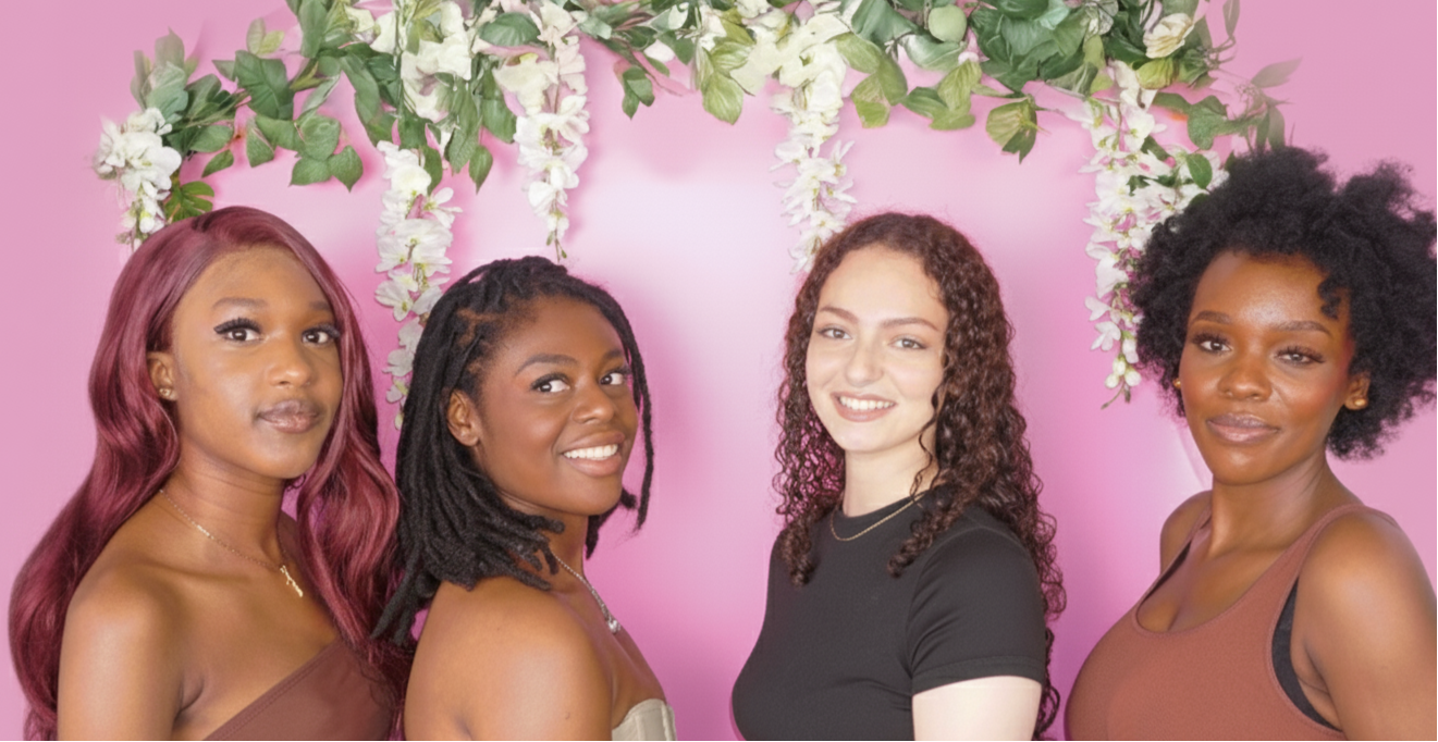 Four women standing together with a floral arch and pink background