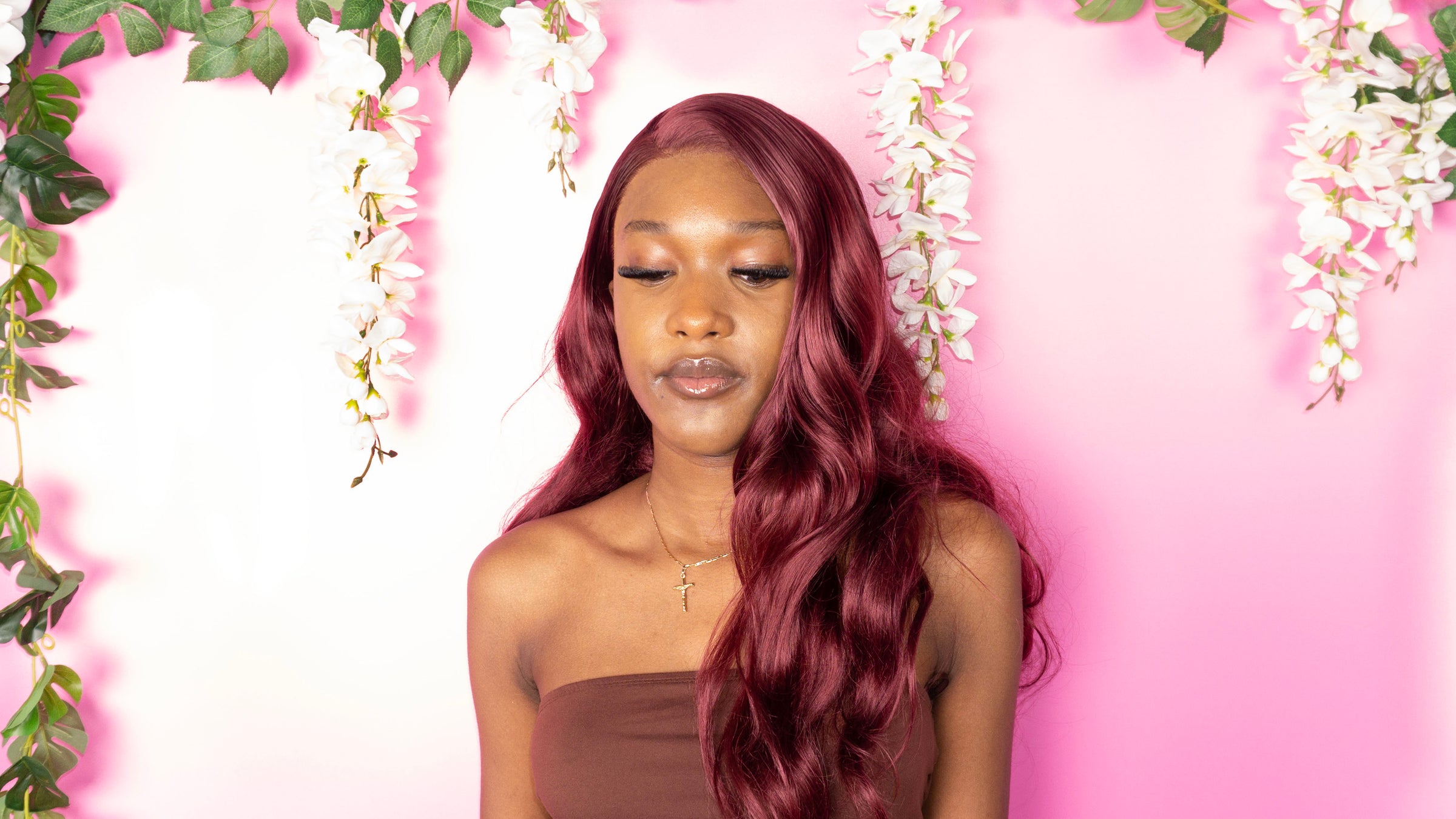 Woman with long burgundy hair against a pink background with floral decorations