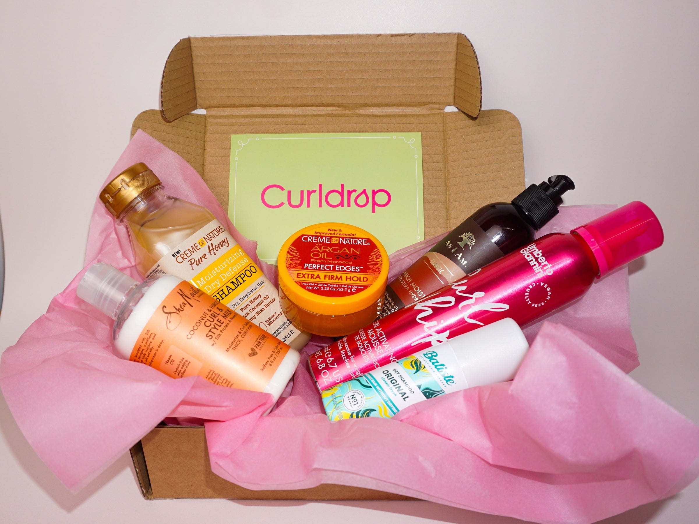 Box of hair care products with a 'Curldrop' brand card on a pink background