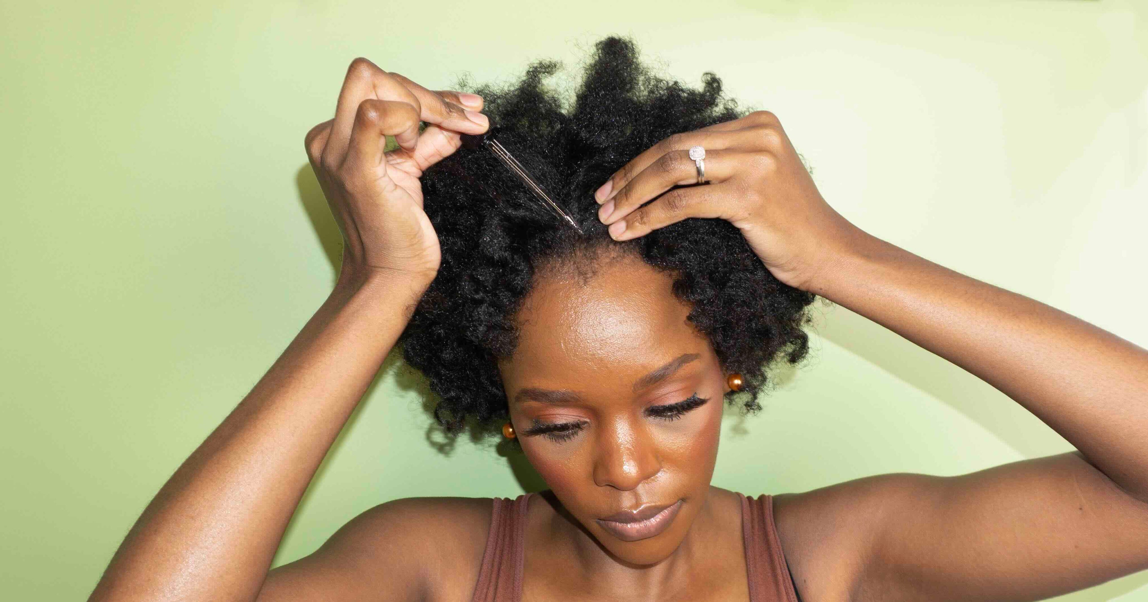 Woman styling her natural hair against a light green background